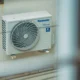 Persona junto a un aire acondicionado bomba de calor portatil con la manguera de evacuación instalada en la ventana y el mando en la mano, ilustrando consejos de compra — Aire acondicionado bomba de calor portatil: claves para elegir bien